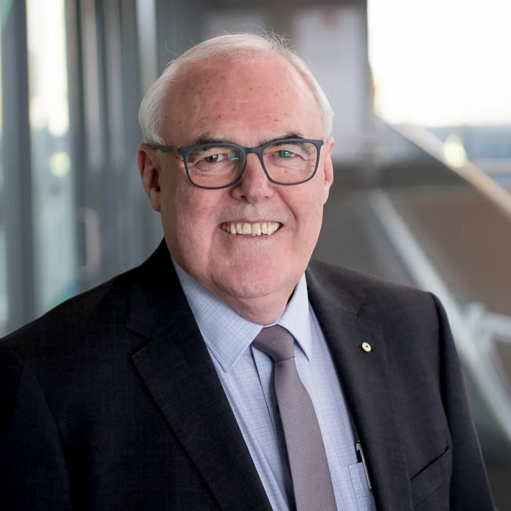 Professional headshot of a man wearing glasses, a dark suit and tie, photographed in a modern office building.