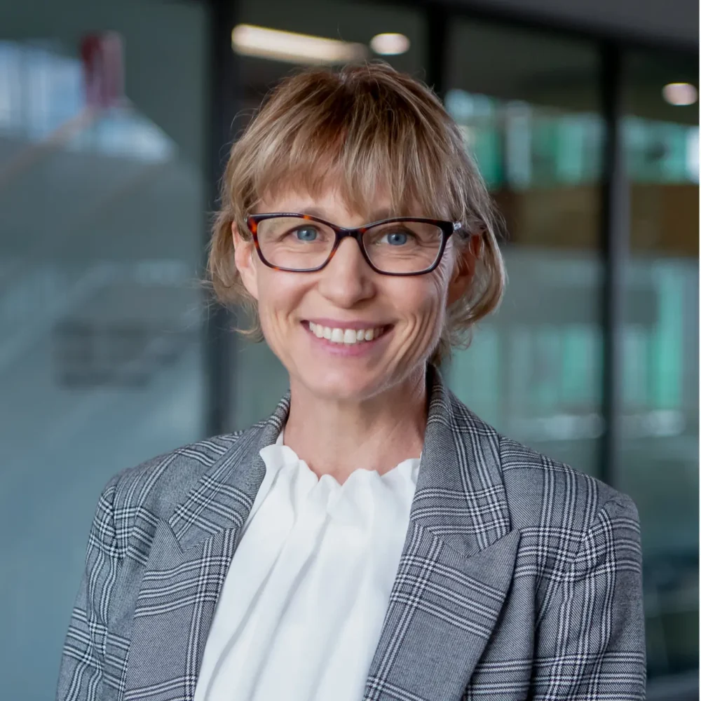 Professional headshot of a smiling woman, photographed in a modern office building.