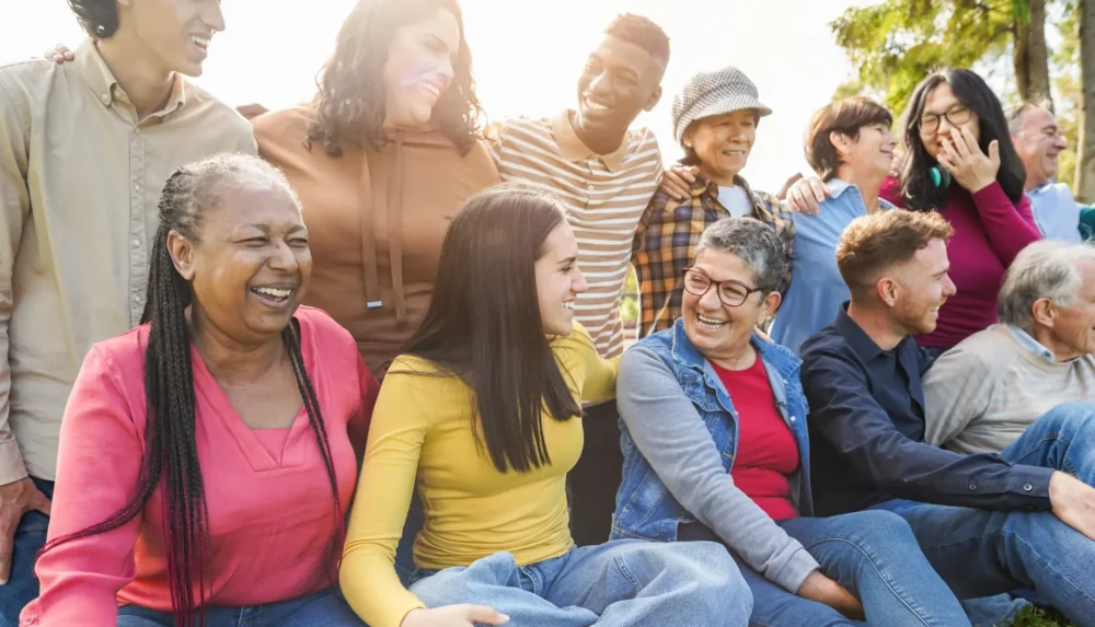 A diverse group of people of different ages and backgrounds laughing and socialising together outdoors.